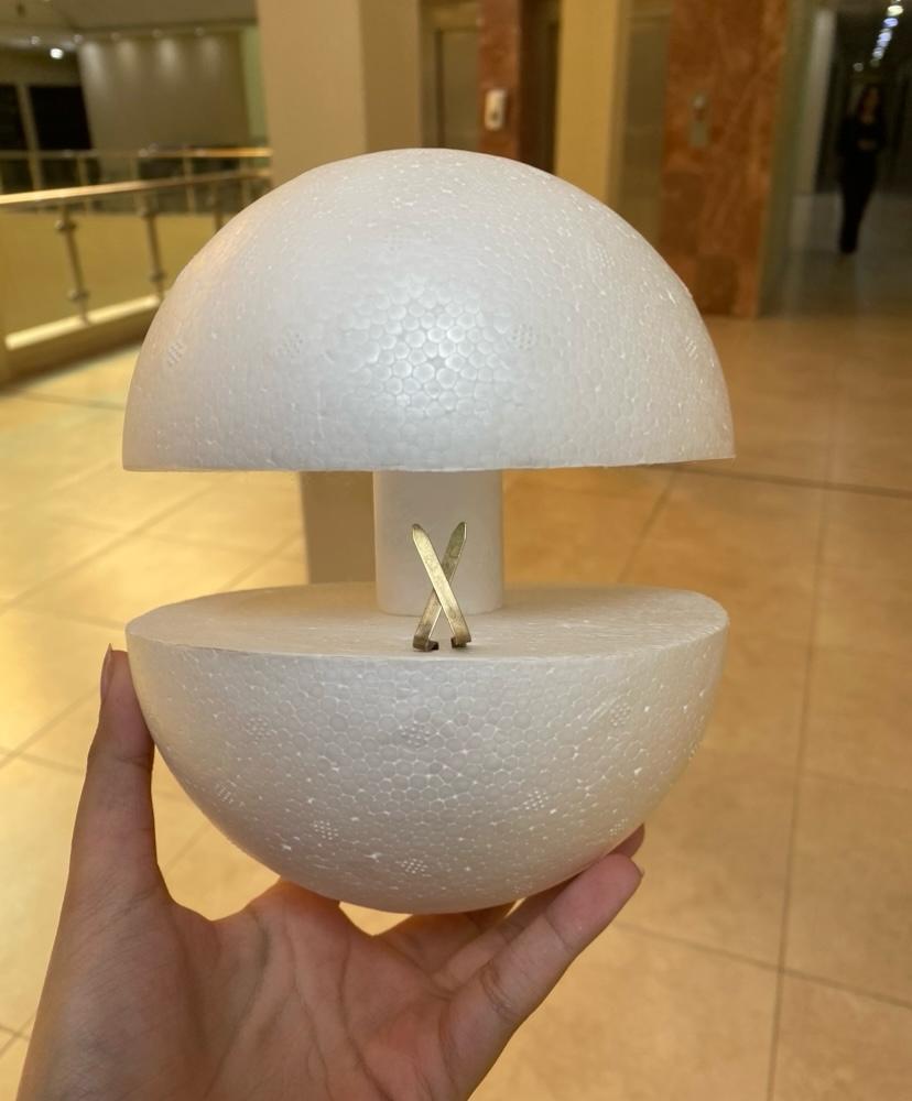 White foam Orbit prototype held in hand, dome lifted to show internal mechanism